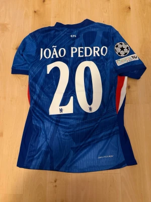 João Pedro #20 – Player Edition (storlek M) - João Pedro #20-tryck. Player Edition med Champions League patch på ärmen. Storlek M. Helt ny och aldrig använd. Säljs i befintligt skick. Skickas snabbt! 🚚💨  Mått för denna tröja (storlek M): (Uppmätta av leverantör – viss variation kan förekomma) • Halva bröstmåttet: 51 cm • Tröjans längd: 72,5 cm • Ärmbredd: 22,5 cm • Axelbredd: 43 cm • Ärmlängd: 39 cm • Manschettbredd: 18 cm  🔥 Player Edition-modell – tajtare passform än vanliga supportertröjor.