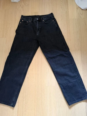 Galaxy Loose Straight Jeans Weekday W29 L32 - Säljer ett par svarta raka jeans från weekday med klassisk femficksmodell och knappgylf. Jeansen har en avslappnad passform och är tillverkade i kraftig denim. Perfekta för dig som gillar en tidlös och enkel stil.