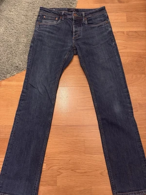 Mörkblå raka jeans  - Säljer ett par klassiska mörkblå jeans från Jack and Jones med raka ben och femficksmodell. Jeansen har snygga kontrastsömmar och en läderpatch bak i midjan. Perfekta till en avslappnad stil och funkar året runt.