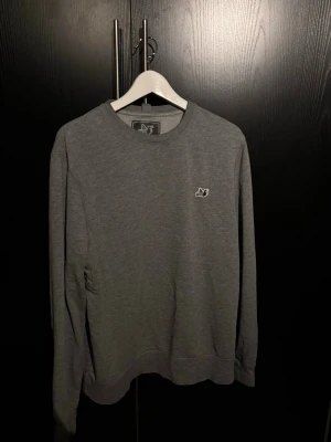 Grå sweatshirt från Peaceful Hooligan - Säljer en stilren grå sweatshirt från Peaceful Hooligan med rund halsringning och deras klassiska duva broderad på bröstet. Tröjan har långa ärmar och är gjord i mjukt bomullsmaterial. Perfekt för en avslappnad look.