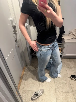 Ljusblå bootcut jeans med låg midja - Säljer ett par ljusblå bootcut jeans med låg midja och klassiska fem fickor. Jeansen har en avslappnad passform och är perfekta för en trendig och avslappnad look. Materialet är denim i bomull. Passar dig som gillar 00-talsstil och vill ha ett par snygga jeans till vardags. Liiitwt hål i bakgfickan som syns på sista bilden. 