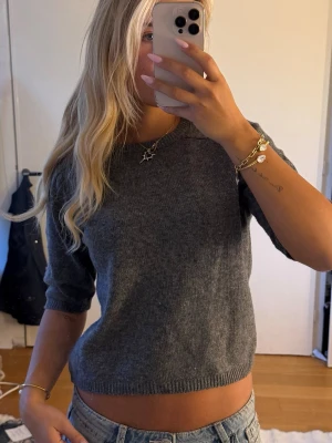 Grå stickad topp med kort ärm - Snygg grå stickad topp med korta ärmar och rund hals. Modellen är något croppad och har ribbstickade muddar vid ärmslut och nederkant.