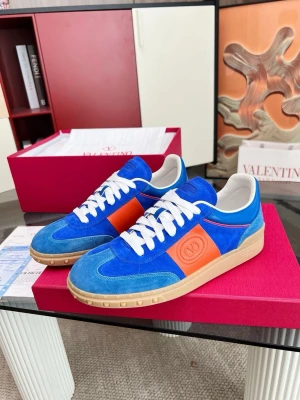 Valentino Garvani Uppvilage - Snygga sneakers från Valentino i blå mocka och orange läderdetaljer. Skorna har vita skosnören, beige sula och klassisk låg siluett. 1.1Valentino-logga på sidan och plös. Perfekta för dig som vill sticka ut med färg och stil.