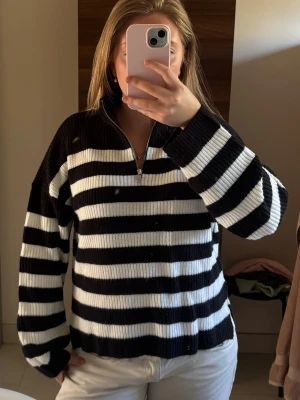 Randig stickad tröja Vero Moda - Säljer en svartvit randig stickad tröja från Vero Moda. Tröjan har halv dragkedja framtill, hög krage och är ribbstickad. Perfekt för dig som gillar klassiska mönster och vill ha en mysig, stilren look.
