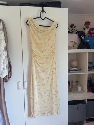 Ljusgul blommig långklänning🫶🏻 - Säljer en ljusgul långklänning med blommigt mönster i pastellfärger. Klänningen har draperad urringning och är ärmlös, vilket ger en elegant och somrig känsla. Perfekt för dig som gillar romantiska och feminina plagg. Nu pris är 500kr! Såååå söt!🤍