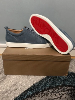 Blåa Christian Louboutin sneakers - Snygga blåa sneakers från Christian Louboutin i mocka med klassisk röd sula och vita kanter. Skorna har lågt skaft, matchande blåa skosnören och en lyxig känsla med bruna detaljer på insidan. Perfekta för dig som vill sticka ut med exklusiv stil.