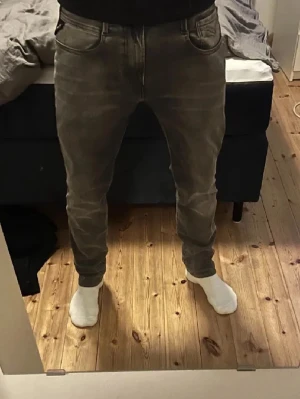 Grå jeans från Replay - Säljer ett par grå jeans från Replay Jeans med snygga slitningar och klassiska fem fickor. Jeansen har coola sömmar på bakfickorna och är perfekta för en avslappnad streetwear eller grisch look. Materialet är mjukt denim med lite stretch för extra komfort. Modellen är anbass och sitter hela perfekt som ni ser på bilden 😊 finns även handgjorda slitningar på jeansen som ej syns så bra vid bild men skickar gärna privat. 