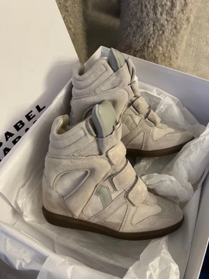 Beige Isabel Marant - Säljer ett par beige höga sneakers från Isabel Marant i mocka och läder. Skorna har chunky design, kardborreband och en cool siluett med inbyggd kilklack. Perfekta för dig som vill ha en statement sneaker med streetstyle-vibe.