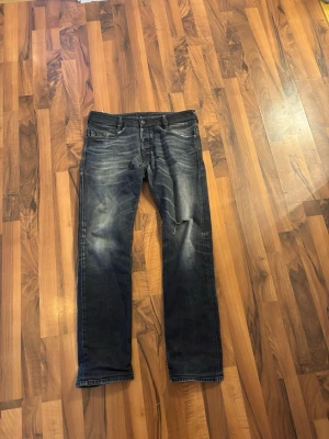 Mörkblå diesel jeans med schyst fade och slitningar  - Säljer ett par mörkblå jeans med slitningar och tvättade detaljer. Jeansen har raka ben, klassisk femficksmodell och en cool, avslappnad look. 
