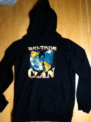 Wu-Tang Clan Huvtröja / Hoodie | M / Medium  - Skön huvtröjja med Wu Tang Clan tryck på framsidan.  Wu-Tang Clan X HM (2022). Medium (Mått finns på bilderna!) 57% bomull. 43% polyester.  Se bilder.