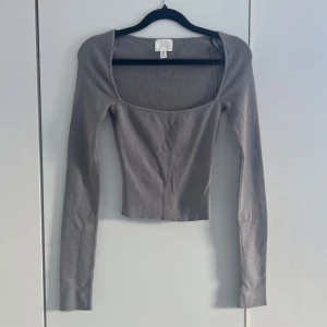 Grå ribbad croppad topp - Trendig grå croppad topp med lång ärm och fyrkantig urringning. Tillverkad i ribbad bomullsmix som ger en slim och bekväm passform. Perfekt att styla med höga jeans eller kjol för en clean look. Knappt använd! 