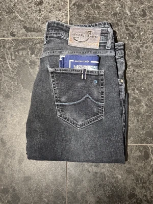 Mörkgrå jeans från Jacob Cohen - Tja! Säljer ett par Snygga mörkgrå jeans från Jacob Cohen med klassisk femficksmodell och kontrastsömmar. Skicket på dessa Jacob Cohen jeans är extremt bra. Storleken är 33! Bara att höra av sig vid eventuella frågor!