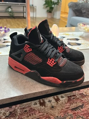 Svarta och röda Air Jordan 4 sneakers - Säljer ett par Air Jordan 4 sneakers i svart mocka med röda detaljer och meshpaneler. Skorna har klassisk siluett, tjock sula och Jumpman-logga på plösen. Snygga detaljer med plast och mesh gör dem riktigt unika för dig som gillar streetwear.