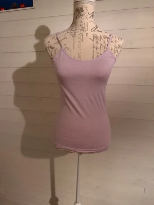 Ljuslila linnetopp med smala band - Säljer en enkel och stilren ljuslila linnetopp med smala axelband. Toppen har en tight passform och är tillverkad i mjuk bomull, perfekt för varma dagar eller som lager under andra plagg.