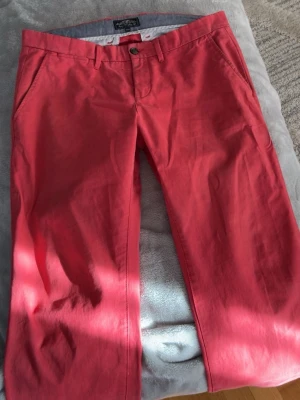 Röda chinos  - Snygga röda chinos med klassisk rak passform och diskreta sidofickor. Tillverkade i mjukt bomullstyg med knappgylf och bälteshällor. Perfekta för dig som vill ha en färgklick i garderoben. Haft i flera år. På bilden ser man lite svart färgning, men syns inte på. Kan sänka pris