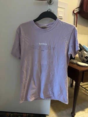 Lila Spiritbox Holy Roller t-shirt - Metalbandet Spiritbox hitlåt Holy Roller som lila T-shirt i small. Stort snyggt tryck på ryggen från musikvideon.. 
