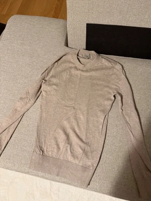 Beige tunn stickad tröja - Säljer en beige tunn stickad tröja med rund halsringning och långa ärmar. Tröjan har en enkel och stilren design med ribbade muddar vid ärmslut och nederkant. Perfekt att matcha med jeans eller kjol för en clean look.