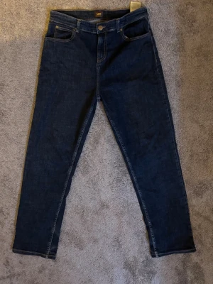 Mörkblå raka jeans från Lee - Snygga mörkblå jeans från Lee med klassisk femficksmodell och raka ben. Jeansen har normal midja, gylf med knapp och dragkedja samt Lee-lapp bak i midjan. Tillverkade i slitstark denim som passar perfekt till vardagslooken.