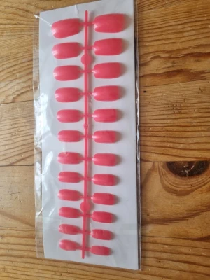 Rosa press-on naglar i kort modell - Snygga press-on naglar i en fräsch rosa färg. Naglarna har en klassisk, något rundad form och kommer på ett ark för enkel applicering. Perfekt för dig som vill fixa naglarna snabbt och smidigt hemma. Materialet är plast.