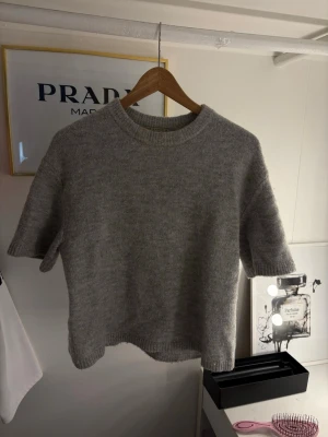 Grå stickad croppad topp - Mysig grå stickad topp med korta ärmar och rund hals. Croppad modell som ger en avslappnad och trendig look. Perfekt att styla med höga jeans eller kjol.