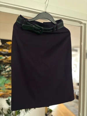 Mörkblå kjol med bälte  - Snygg mörkblå kjol med ett grönt bälte i midjan. Kjolen har en rak, klassisk form och är perfekt för dig som gillar stilrena plagg. Tillverkad i Tyskland och passar till många olika looks.