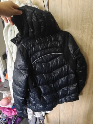 Svart dunjacka från EA7 Emporio Armani Helg REA NU! - Snygg blå & svart dunjacka från EA7 Emporio Armani med quiltad design och huva. Jackan har en diskret logga på bröstet och reflekterande detalj på ryggen. Perfekt för kalla vinterdagar och riktigt stilren look.