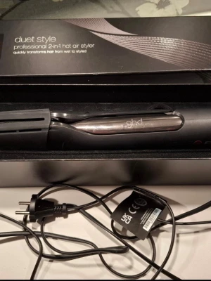 ghd Duet Style 2-i-1 varmluftsborste - Säljer en svart ghd Duet Style, en professionell 2-i-1 varmluftsborste som både torkar och stylar håret. Den har en elegant design med metalliska detaljer och levereras med originalkartong och skyddshölje. Perfekt för att snabbt fixa frisyren hemma.