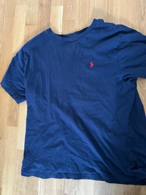 Mörkblå t-shirt från Polo Ralph Lauren - Klassisk mörkblå t-shirt från Polo Ralph Lauren med röd broderad logga på bröstet. T-shirten har rund halsringning och korta ärmar. Tillverkad i mjuk bomull som känns skön mot huden. Perfekt till jeans eller shorts.