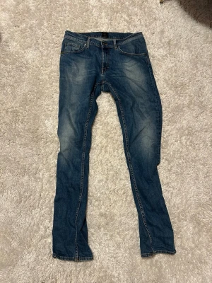 Blå slim fit jeans med slitningar - Säljer ett par blå slim fit jeans med snygga slitningar och klassisk femficksdesign. Jeansen har kontrastsömmar och normal midja. Materialet är denim i bomull och passformen är smil fit.