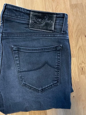 Svarta från Jacob Cohen - Snygga mörkblå jeans från Jacob Cohen med klassisk femficksdesign och svart patch bak i midjan. Jeansen har raka ben och är tillverkade i ett mjukt denimtyg som ger en skön passform. Perfekta för en stilren och avslappnad look. Lagning kolla bild