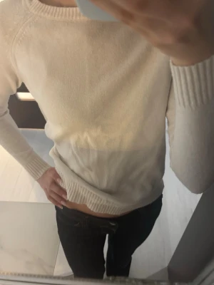 Ljus stickad tröja med rund hals - En enkel och stilren beige/vit stickad tröja med rund halsringning och långa, tighta ärmar. Tröjan har ribbade muddar vid ärmslut och nederkant, vilket ger en snygg och avslappnad look. Skriv till mig vid frågor eller intresse 