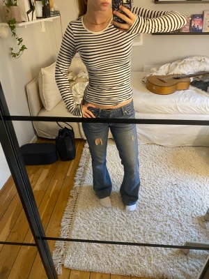 Randig långärmad topp - Säljer en slim-fit långärmad topp som är randig med vit och svarta sträck. Toppen har rund halsringning och är gjord i ett mjukt, stretchigt material som sitter tight mot kroppen. 