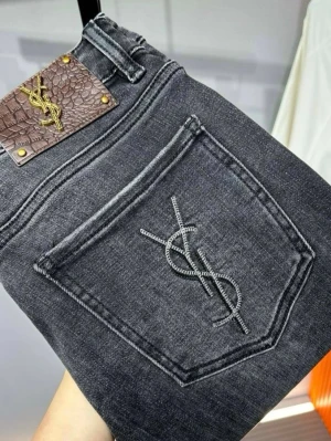 Svarta jeans från Yves Saint Laurent - Säljer ett par svarta jeans från Yves Saint Laurent med ikonisk YSL-logga broderad på bakfickan och ett brunt lädermärke med gulddetaljer i midjan. Jeansen har klassisk femficksdesign och är tillverkade i denim med snygg tvätt.
