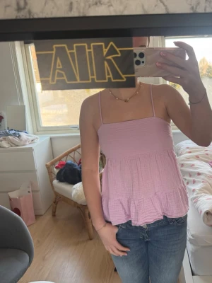 Rosa topp med knyt i ryggen - Supersöt rosa topp med tunna axelband och volangkant. Toppen har öppen rygg med snygg knytning och luftig passform🩷 Älskar denna tröjan men den passar inte mig längre!