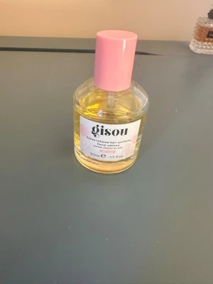 Gisou Honey Infused Hair Perfume - Gisou Honey Infused Hair Perfume i limited edition. Flaskan är rund i genomskinligt glas med en ljusgul vätska och ett rosa lock. Innehåller 50 ml och har en söt, fräsch doft med inslag av honung. Perfekt för dig som vill ge håret en extra boost av doft.