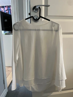 Vit blus från KappAhl,  - Säljer en stilren vit blus från KappAhl i storlek 40. Blusen har lång ärm, rund halsringning och dubbla lager vid fållen för en snygg layering-effekt. Materialet är lätt och flowy, perfekt för en clean och fräsch look. Jag har normalt stl 36 men på mig passar den ändå bra, den blir lite mer oversized:)