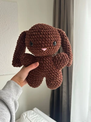 Brun virkad kanin - Virkat gosedjur i velvetgarn. Kaninen är 26cm lång och tillverkad för hand, vilket gör varje kanin unik.  Kaninen har svarta säkerhetsögon som sitter fast från insidan. Rekommenderas dock inte för de allra minsta barnen, då det alltid finns en viss risk, vid hårt drag, att de lossnar.  Perfekt som present eller mysig inredningsdetalj!  Tvättråd: max 30°C, handtvätt.