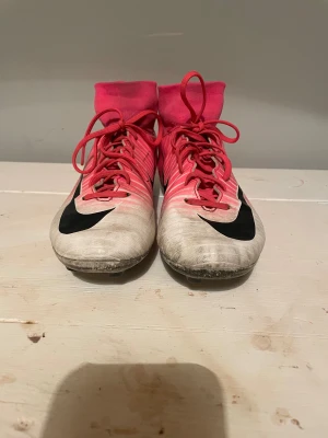 Nike Mercurial rosa fotbollsskor - Säljer ett par Nike Mercurial fotbollsskor i rosa med svarta detaljer och vita inslag. Skorna har högt skaft i stretchigt material, snörning och dobbar för bra grepp på planen. 