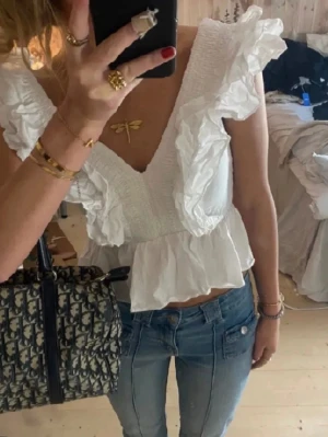 Vit volangblus från h&m - Säljer denna populära vita toppen med breda volangdetaljer längs axlar och urringning. Toppen har v-ringad hals, smockad överdel och peplum nedtill. Toppen är i fint skick (det 2 första bilderna är lånade)💕💕💗