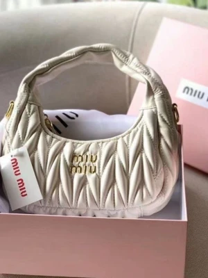 Vit quiltad handväska från Miu Miu - Supersnygg vit handväska från Miu Miu med quiltat mönster och guldfärgade detaljer. Väskan har en rundad form och ett kort handtag, perfekt för att bära på axeln. Tillverkad i mjukt läder och pryds av Miu Miu-loggan i guld framtill.