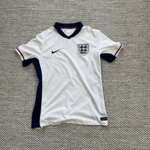 England Nike fotbollströja vit - Orginal England 2024 EM fotbollströja från Nike med mörkblå detaljer längs sidorna och kragen. Tröjan köpt på unisport för 1500kr storlek M (inget namn på ryggen). Man kan trycka själv nu om man vill. Använd 1 gång