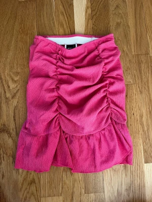 Rosa volangkjol från Gina Tricot - Supersnygg rosa kortkjol från Gina Tricot med volangdetaljer och rynkade partier framtill. Kjolen har en figurnära passform och är tillverkad i ett mjukt, strukturerat material som känns bekvämt mot huden. Perfekt för dig som vill sticka ut lite extra. Aldrig använd men bortplockad lapp.