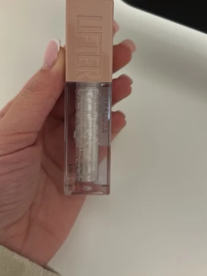 Maybelline Lifter Gloss 001 Pearl - Säljer ett Maybelline Lifter Gloss i färgen 001 Pearl. Läppglanset har en transparent, pärlvit nyans med skimrande effekt och kommer i en stilren fyrkantig förpackning med beige lock. Innehåller hyaluronsyra för extra återfuktning.