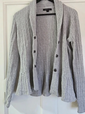 Ljusgrå ribbad kofta från mywear woman - Säljer en ljusgrå ribbad kofta från mywear woman. Koftan har långa ärmar, knappar framtill och en bred krage. Materialet är mjukt och stretchigt, perfekt för lager på lager. Passar dig som gillar en avslappnad men ändå stilren look.