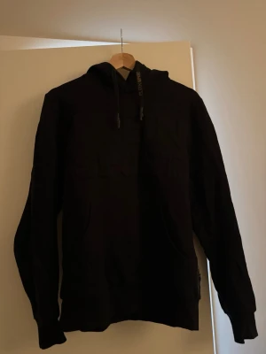 Svart Philip plein spirt hoodie  med huva och ficka - Säljer en Philipp plein sport svart hoodie med klassisk huva och dragsnören. Hoodien har en stor magficka framtill och ribbade muddar vid ärmar och nederkant. Text på tröjan. Med logo på armen. Bra skick. Storlek S.