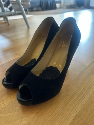 Svarta peep-toe pumps Louboutin  - Snygga svarta pumps från Christian Louboutin med peep-toe och platåsula i storlek 40. Skorna är i mocka med läderdetaljer och har klassisk siluett. Har non slip sticker på dem men det går att ta bort.  Köpte dem på vinted men senare insåg att det var oberkväma för min fot. Osäker att det är original!
