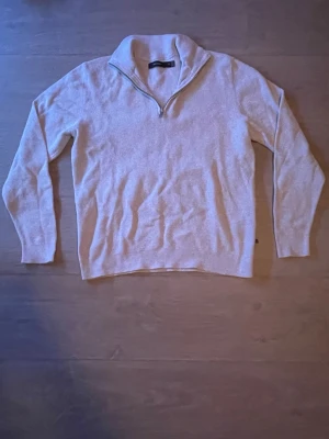 Beige stickad tröja med halvzip från Matinique  - Säljer en beige stickad tröja från Matinique med halvzip och hög krage. Tröjan har långa ärmar och ribbade muddar vid ärmslut och nederkant. Perfekt för lager på lager och enkel att matcha med olika outfits.