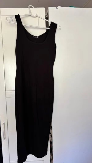 Svart basic klänning - Säljer en svart, ärmlös klänning från Boohoo med figurnära passform, rundad halsringning och slits. Klänningen i stretchigt material som formar sig efter kroppen. Perfekt basplagg. 