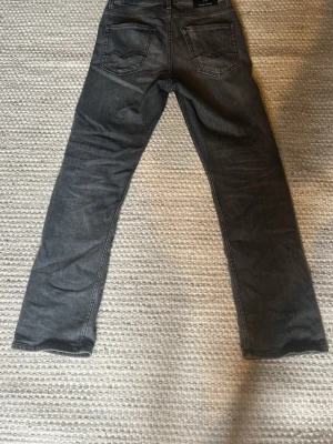 Grå Replay Thad Jeans - Säljer ett par grå jeans från Replay med rak passform och klassisk femficksdesign. Jeansen har subtila slitningar och är tillverkade i mjuk denim. Perfekta för en avslappnad och stilren look.
