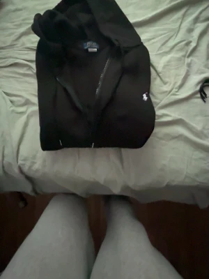 Svart hoodie från Polo Ralph Lauren - Säljer en svart hoodie från Polo Ralph Lauren med dragkedja och klassisk huva. Tröjan har det ikoniska vita Polo-märket broderat på bröstet och dragsko i huvan. Perfekt för en chill och stilren look.